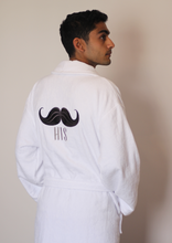 Load image into Gallery viewer, Man wearing white bathrobe with icon of mustache on its back and &quot;his&quot; written under it. He has both his hands in his pockets. Egyptian Cotton bathrobe. 